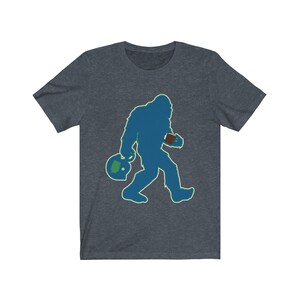 K&ouml;nnte beinhalten: Ein dunkelblaues T-Shirt mit einer gr&uuml;n-blauen Silhouette von Bigfoot, der einen Football und einen Helm tr&auml;gt.