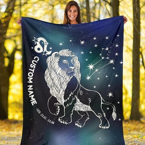 May include: A blue and green fleece blanket with a white outline of a lion and the constellation Leo. The blanket has a starry background and the text "CUSTOM NAME" and "LEO 23.07 - 23.08" printed on it.