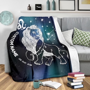 May include: A soft, blue and green throw blanket with a white outline of a lion and stars. The text "CUSTOM NAME" and "LEO 23.07 - 23.08" is printed on the blanket.