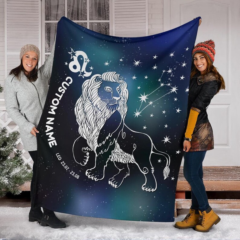 May include: A blue fleece blanket with a white outline of a lion and stars. The text "CUSTOM NAME" is written vertically on the left side of the blanket. The text "LEO 23.07. - 23.08." is written below the lion.