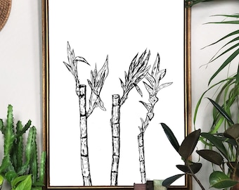 May include: A black and white line drawing of three bamboo plants in a gold frame. The frame is hanging on a white wall above a wooden dresser with two drawers. There are two small wooden statues and a stack of books on the dresser.