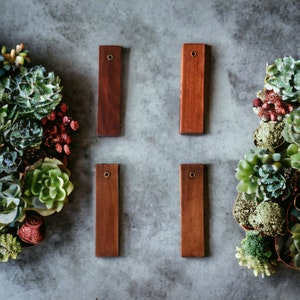 May include: Four rectangular wooden tags with brass eyelets. The tags are a dark reddish brown color and are arranged in a grid pattern.