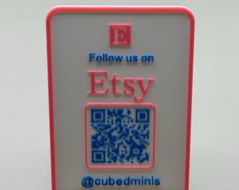 May include: A rectangular sign with a pink border and a white background. The sign features the text "Follow us on Etsy" in blue and pink, along with a QR code and the username "@cubedminis". The sign is displayed on a white stand.