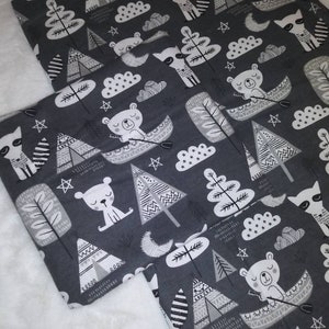 Puede incluir: Tela gris con un estampado blanco de osos, mapaches, árboles y tiendas de campaña. La tela tiene un tema de bosque.