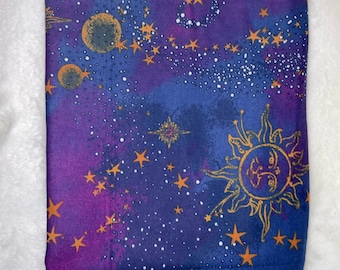 Könnte beinhalten: Lila und blauer Stoff mit einem himmlischen Muster mit goldenen Sternen, einer Sonne und Monden. Der Stoff hat einen aquarellartigen Effekt.