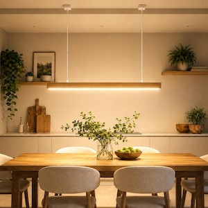 May include: A linear wooden pendant light fixture suspended by two white cords above a rectangular wooden dining table. The light features a long, horizontal wooden housing with an integrated LED strip that emits a warm, downward-facing glow.