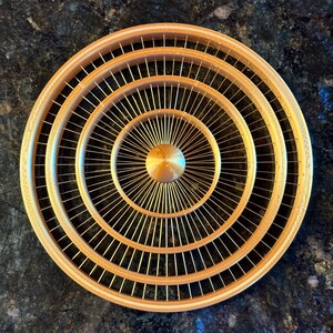 May include: A gold-colored, circular decorative object with a series of concentric rings and radial spokes. The design features intricate detailing and a central hub. The object is likely a decorative piece or part of a larger design.