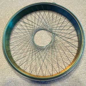 May include: A bicycle wheel with a gradient of colors, transitioning from blue to green and gold. The wheel's rim has a textured pattern, and numerous silver spokes converge towards the center.