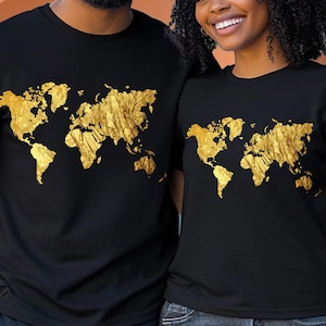 Puede incluir: Camisetas negras con un diseño de mapa del mundo dorado. El gráfico muestra los continentes en detalle. Las camisetas son de manga corta y parecen estar hechas de un material suave. El diseño es dorado.