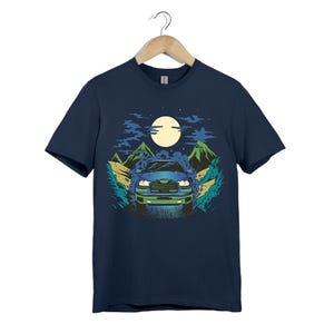 Puede incluir: Camiseta azul marino con un gráfico de un camión azul conduciendo por un paisaje montañoso bajo una luna llena. El diseño incluye acentos verdes y azules, creando una ilustración escénica.