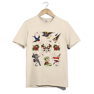Könnte beinhalten: Ein beiges Kurzarm-T-Shirt mit einem Grafikdruck im traditionellen Tattoo-Stil, bestehend aus einer Schwalbe, einem Adler, einem geflügelten Totenkopf, Rosen, einem Zuckerschädel, einem schwarzen Panther, einer Kobra und einem Dolchherz.
