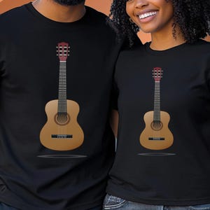 Pode incluir: T-shirts pretas com um desenho de guitarra. A guitarra é castanha clara com um cabeçote vermelho escuro e uma escala preta. As camisas são de manga curta e têm gola redonda.