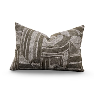 May include: A rectangular decorative pillow with a geometric pattern in shades of olive green and gray. The pillow has a textured appearance, with a mix of vertical and horizontal lines and shapes. The pillow is designed for home decor.
