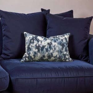 K&ouml;nnte beinhalten: Ein marineblaues Sofa mit mehreren passenden Kissen. Ein Kissen hat ein abstraktes blau-wei&szlig;es Muster. Die anderen Kissen sind einfarbig marineblau. Das Sofa und die Kissen sind aus einem weichen, strukturierten Stoff.