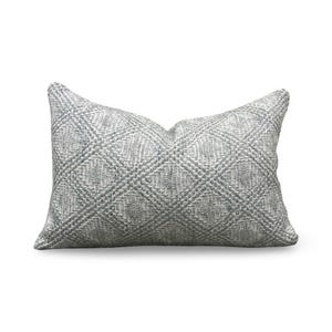 May include: A rectangular throw pillow featuring a textured, woven fabric in shades of light gray and white. The surface displays a repeating diamond pattern created by raised, thick yarn stitches that provide a tactile, dimensional appearance.