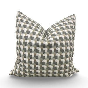 May include: A decorative square pillow with a woven pattern in shades of gray, white, and tan. The pillow has a textured appearance and is designed for home decor.