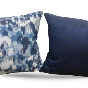 K&ouml;nnte beinhalten: Zwei dekorative Kissen. Ein Kissen hat ein blau-wei&szlig;es abstraktes Muster. Das andere Kissen ist einfarbig marineblau. Beide Kissen sind rechteckig und scheinen aus weichem Stoff zu sein.