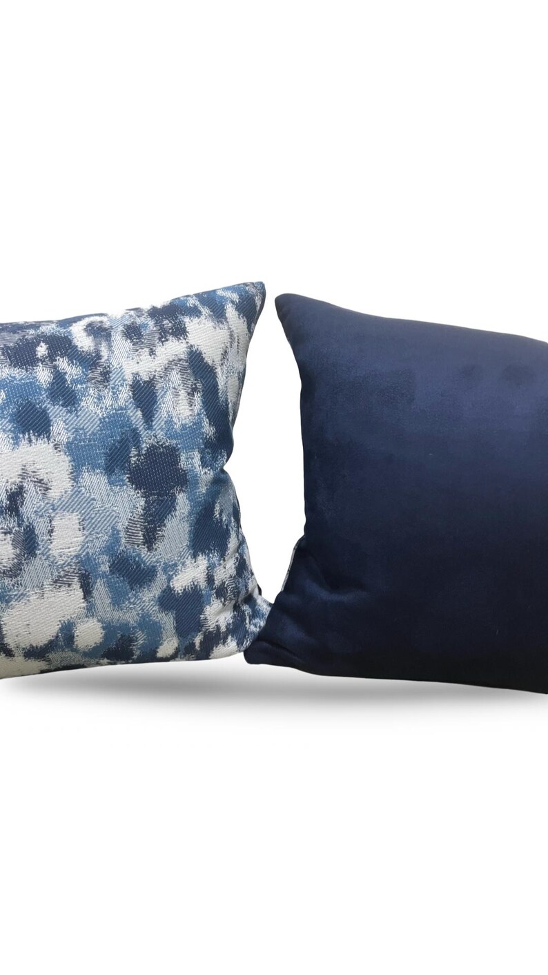 K&ouml;nnte beinhalten: Zwei dekorative Kissen. Ein Kissen hat ein blau-wei&szlig;es abstraktes Muster. Das andere Kissen ist einfarbig marineblau. Beide Kissen sind rechteckig und scheinen aus weichem Stoff zu sein.