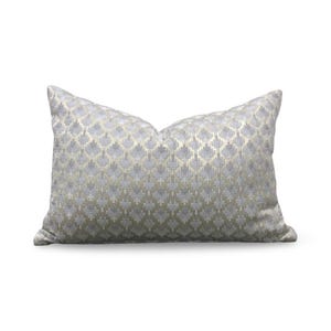 May include: A rectangular throw pillow featuring a repeating geometric pattern in shades of light gray and metallic gold. The fabric has a subtle sheen and a textured appearance, with the pattern consisting of small, interlocking cross-like shapes.