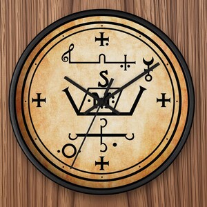 May include: A round wall clock with a black frame and a beige parchment-style face. The clock features black hands and a central black sigil design with various symbols, including crosses, a crescent moon, and the letter S, printed in black ink.
