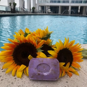 May include: A purple bar of soap with the words "Lavender Honey" embossed on it, surrounded by yellow sunflowers.