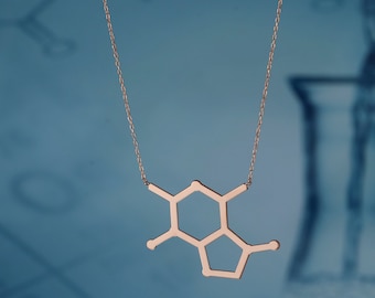 May include: A rose gold necklace featuring a molecular structure pendant. The pendant is a geometric design with a chain. The necklace is displayed against a blue background with blurred scientific imagery.