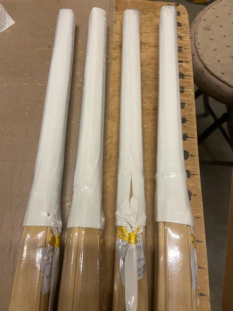 May include: Four wooden sticks wrapped in white plastic with gold ribbon. The sticks are bundled together and have a white label with black text.