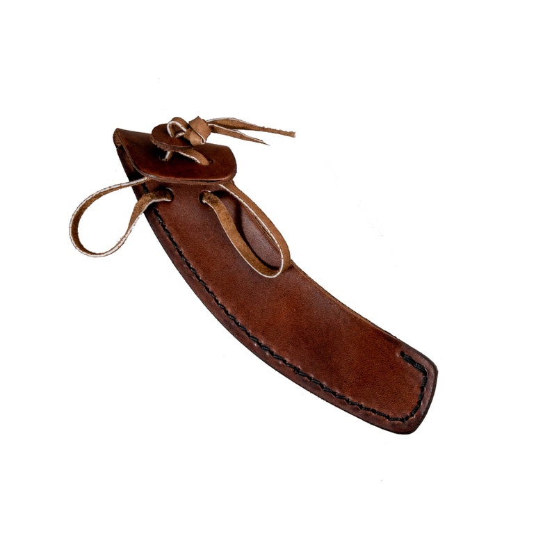 May include: A brown leather sheath with a tan leather strap and buckle. The sheath has a stitched edge and is designed to hold a knife or other small tool.