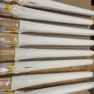 May include: A stack of white wrapped wooden dowels with yellow tape on the ends. The dowels are stacked on a brown surface.