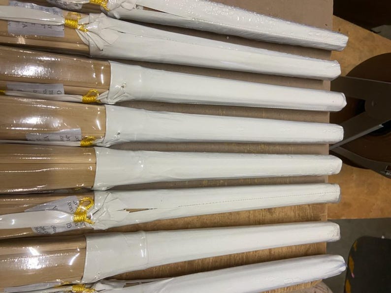 May include: A stack of white wrapped wooden dowels with yellow tape on the ends. The dowels are stacked on a brown surface.