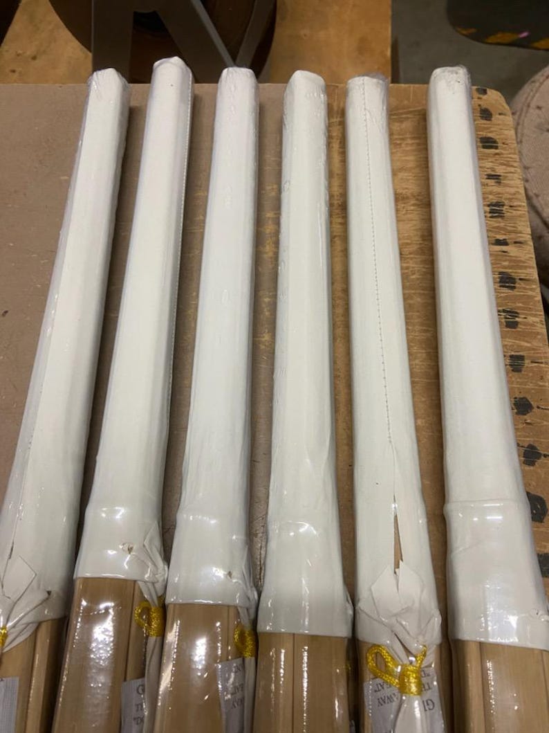 May include: Six wooden dowels wrapped in white paper with gold accents. The dowels are bundled together and ready to be used for crafts or other projects.