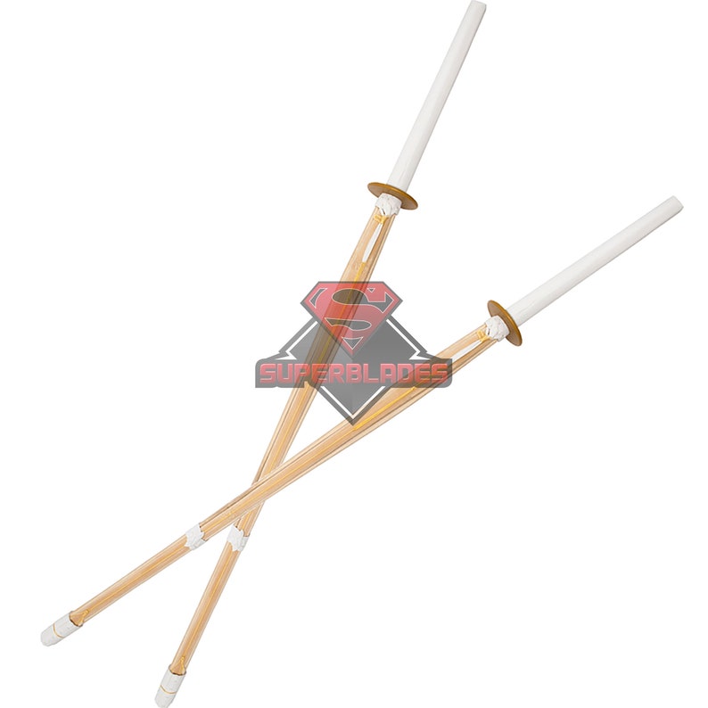 May include: Two wooden practice swords with white padded tips, crossed over each other. The swords are made of bamboo and have a natural wood finish.