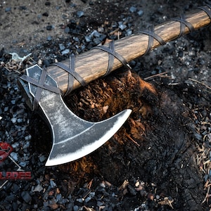 May include: A black axe with a wooden handle wrapped in leather. The axe is resting on a charred tree stump.