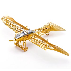 May include: A gold metal model of a vintage airplane with a silver metal cockpit. The model is detailed with a wire frame design and has a propeller.