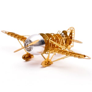 May include: A gold metal model airplane with a silver propeller and a detailed, open-frame design. The model is on a white background.