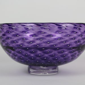 May include: A purple glass bowl with a textured surface and a small foot. The bowl has a speckled appearance.