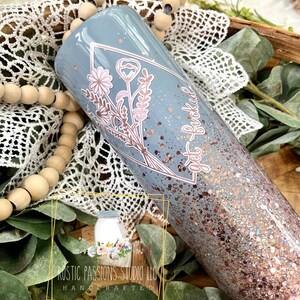 May include: A light blue tumbler with a floral design and the text "get buckled" in rose gold glitter. The tumbler is covered in rose gold glitter.