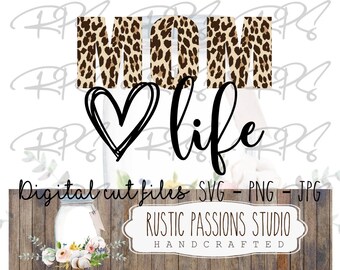May include: A digital cut file design featuring the words "MOM life" in black script font. The word "MOM" is in leopard print with brown and tan spots. A black hand-drawn heart is between the words.