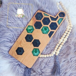 May include: A wooden cutting board with a green and black epoxy resin inlay in a honeycomb pattern. The board has a handle on the side and is handmade.