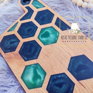 May include: A wooden cutting board with a honeycomb design. The honeycomb is filled with green and blue epoxy resin. The board is handcrafted and has a rustic look.  RUSTIC PASSIONS STUDIO LLC HANDCRAFTED