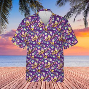 May include: Purple short-sleeve button-down shirt with a repeating pattern of yellow trombones, flowers, and leaves. The shirt has a classic collar and is made of a lightweight fabric, perfect for warm weather. The background shows a tropical beach scene.