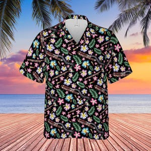 May include: Black short-sleeved button-down shirt with a tropical floral and musical instrument pattern. The design features pink, blue, and yellow flowers, green leaves, and brown musical instruments. The shirt has a classic collar and a relaxed fit.