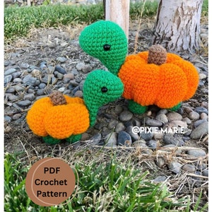 May include: Two crocheted pumpkin turtles, one larger than the other, are sitting on a bed of green grass. The turtles are green with orange pumpkins for shells. The smaller turtle is in front of the larger turtle. The text "PDF Crochet Pattern" is visible in the lower left corner of the image.