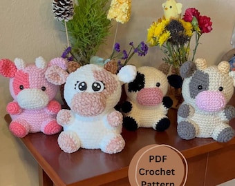 May include: A PDF crochet pattern for making adorable crocheted cow plushies. The pattern includes four different color variations: pink, white, cream, and gray. The cows are sitting on a wooden table with a vase of flowers in the background.