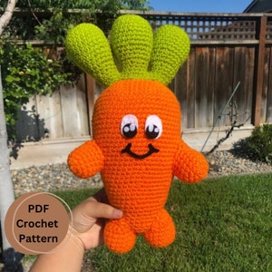 Peut inclure: Un jouet en crochet en forme de carotte avec un dessus vert et un visage souriant. La carotte est orange et a des yeux blancs et une bouche noire. Le jouet est tenu dans une main. Modèle de crochet PDF.