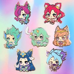 以下が含まれることがあります： 大きな目と詳細な衣装を持つ、アニメスタイルのキャラクターが特徴の、7つのカラフルなエナメルピンのコレクション。各ピンは金色の輪郭を持ち、ユニークな髪とアクセサリーを持つ異なるキャラクターを描いています。背景は青と紫のグラデーションです。