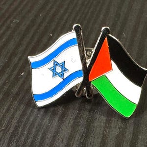 May include: A pin with two crossed flags. The flag on the left is the Israeli flag, with a blue Star of David on a white field with two blue stripes. The flag on the right is the Palestinian flag, with three horizontal stripes of black, white, and green, and a red triangle on the hoist side.