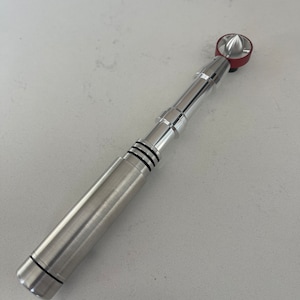 May include: A silver-colored, cylindrical device with a red top and black bands. The device has a metallic finish and a conical tip. The design is sleek and modern, with a focus on clean lines and a polished appearance.