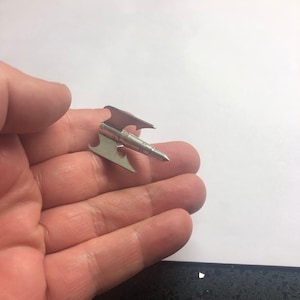 Op de afbeelding: Een zilveren pijlpunt met een scherpe punt en een brede, platte basis. De pijlpunt is ontworpen voor gebruik met een boog en pijl.