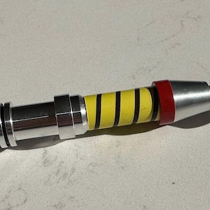 May include: A silver and red disassembled sonic screwdriver with a yellow and black striped section.